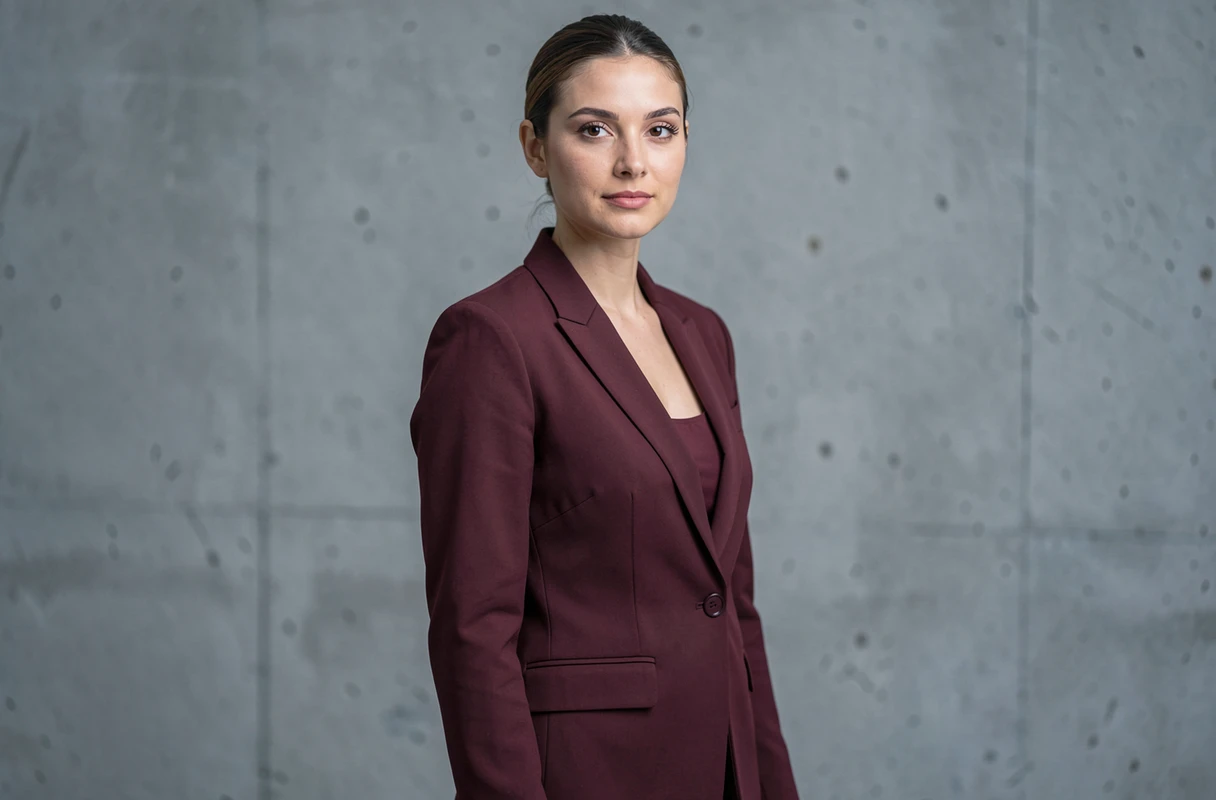 Portrait éditorial féminin en plan américain avec blazer bordeaux sur fond béton neutre